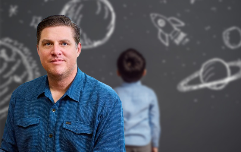 Dr. David Yaeger, in front of a child standing at a chalkboard with drawings of rockets and planets