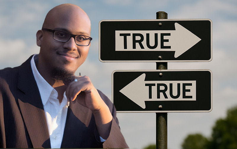 Jason Craige Harris in front of two street signs pointing in different directions but which both read 'true'